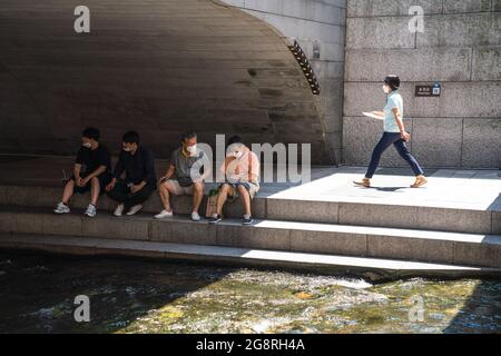 Seoul, Südkorea. Juli 2021. Um den Cheonggyecheon Stream in Seoul herum sitzen Menschen, die Gesichtsmasken tragen, als vorbeugende Maßnahme gegen die Ausbreitung des Coronavirus. (Foto von Simon Shin/SOPA Images/Sipa USA) Quelle: SIPA USA/Alamy Live News Stockfoto