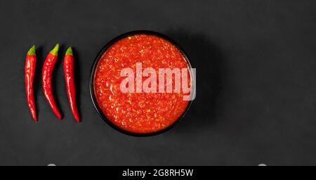 Adjika auf schwarzem Hintergrund. Scharfe Chilischoten, Harissa-Sauce. Hausgemachte Rose Harissa in einer Schüssel. Platz zum Kopieren, Draufsicht, flach liegend. Stockfoto