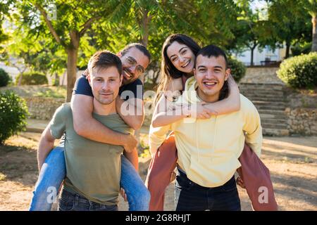 Gruppe von kaukasischen Freunden, die Spaß im Park haben. Sie sind glücklich und lachen. Sie tragen farbenfrohe Kleidung. An einem sonnigen Tag. Sie sind oben auf Stockfoto