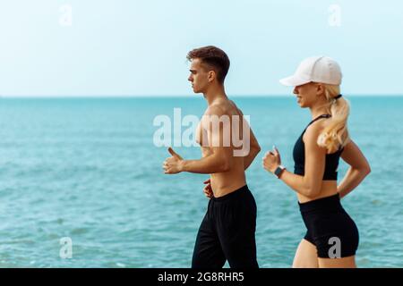 Junges Fitness-Paar, Mann und Frau laufen am Wasser entlang, Athleten joggen früh am Morgen, Fitness im Freien, Training während Isolat Stockfoto