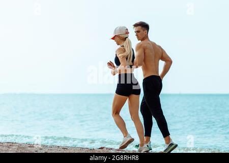 Junges Fitness-Paar, Mann und Frau laufen am Wasser entlang, Athleten joggen früh am Morgen, Fitness im Freien, Training während Isolat Stockfoto