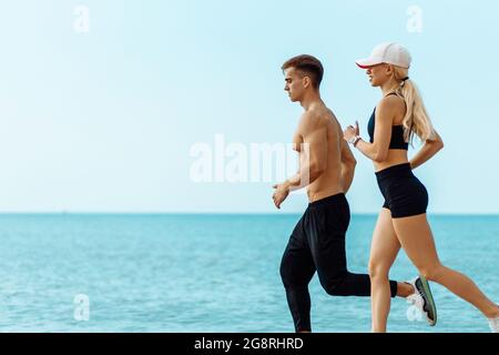 Junges Paar läuft am Strand, Athletic Attraktive Menschen Joggen in Sommer-Sportbekleidung, am Meer, Ausübung ihrer gesunden Lebensweise Stockfoto