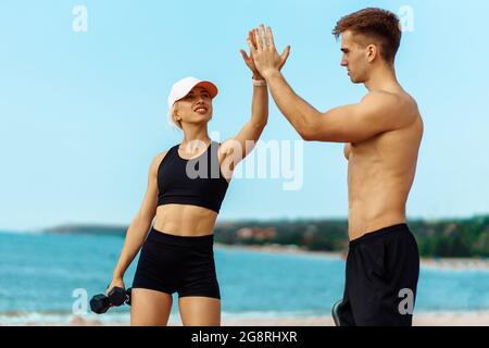 Sportlich muskulöser Mann und Fitness-Frau geben sich gegenseitig eine hohe fünf, Fitness-Menschen nach einem erfolgreichen Training am Meer am Morgen Stockfoto