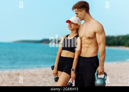 Schöne junge sportliche Paar Training mit Hanteln, tun Sportübungen am Strand, Sport paar Training mit Hanteln, muskulösen Mann und Stockfoto