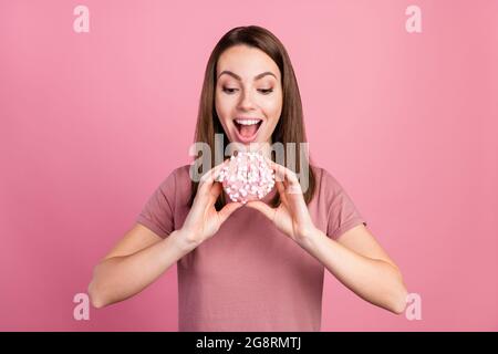 Portrait von attraktiven hungrigen fröhlichen Mädchen essen frischen Donut isoliert über rosa Pastellfarben Hintergrund Stockfoto