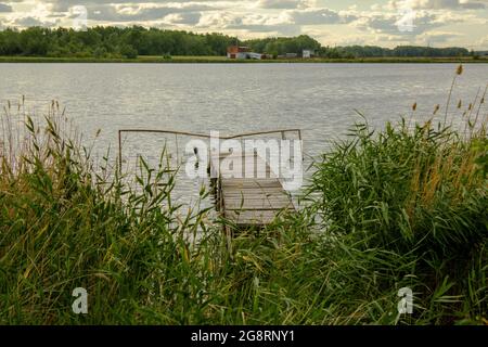 Blick durch das Schilf auf die alte Fischerbrücke. Ein See, der von vielen Stadtbewohnern für ein Wochenende in der Nähe des Dorfes genutzt wird. Stockfoto