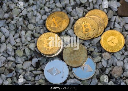 Viele wertvolle Gold- und Silbermünzen Bitcoin Ether und ada aus Kryptowährung liegen auf weißem Kies Stockfoto