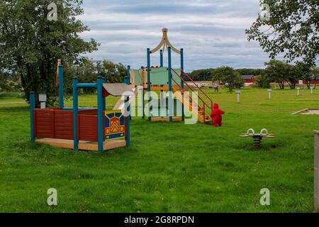 Ein Kind in roten Overalls auf einem Spielplatz auf grünem Gras. Gemeinsamer Zeitvertreib von Eltern mit einem Kind im Freien an der frischen Luft. Stockfoto