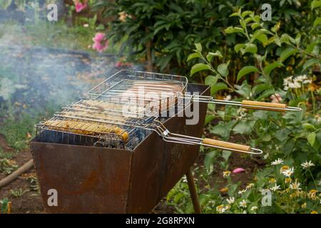 Zwei Grills mit Fleischwürsten und Hähnchenhacken auf einem Grill. Stockfoto