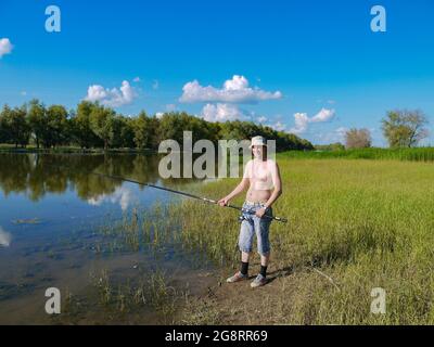 Ein Mann mit einer Angelrute fischt auf einem Fluss im Dorf. Das Konzept eines gesunden Lebensstils in der Natur. Stockfoto