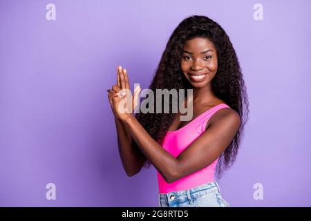 Foto von jungen attraktiven afrikanischen Mädchen glücklich positive Lächeln Geste Hände Pistole verspielt isoliert über lila Farbe Hintergrund. Stockfoto