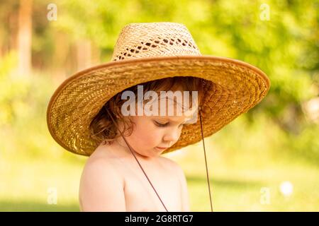 Ein kleines weißes Kind in einem Strohhut schaut nach unten. Die süßen Momente der Kindheit auf der Ranch. Stockfoto