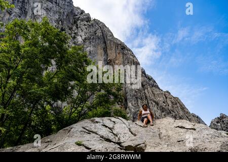 STARI GRAD, KROATIEN - 18. Jul 2021: Eine Frau, die auf einem hohen Felsen in einem Berg im Nationalpark Paklenica sitzt. Stockfoto