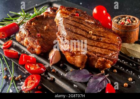 Geröstete Fleischstücke mit Gemüse und Gewürzen auf schwarzem Hintergrund. Saftige Fleischstücke vom Grill mit Paprika, Rosmarin, Tomate, Pfeffer, Lorbeerblatt... Stockfoto