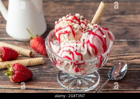 Erdbeer-, Banane- und Rahm-Roma-Eis in einer Glasschüssel mit roter Sauce darüber gegossen. Stockfoto