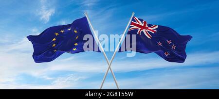 Flaggen der Europäischen Union und Neuseelands winken im Wind auf Fahnenmasten gegen den Himmel mit Wolken am sonnigen Tag. Symbolisieren Beziehung, Dialog zwischen Stockfoto