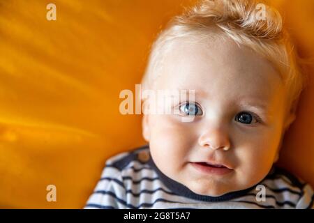 Nahaufnahme eines niedlichen 9 Monate alten Jungen mit blauen Augen auf einem gelben Hintergrund Stockfoto