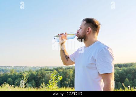 Der bärtige Mann mittleren Alters trinkt am heißen Sommertag Wasser aus der Flasche Stockfoto