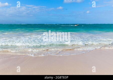 An einem sonnigen Tag fährt ein kleines Motorboot entlang des Bavaro-Strandes, der Küstenlandschaft der Dominikanischen Republik Stockfoto