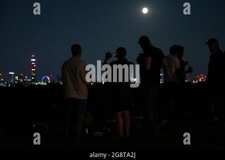 Die Menschen auf Primrose Hill beobachten, wie der Mond über dem Zentrum Londons aufgeht. Der Juli-Vollmond, auch bekannt als der Donnermond, ist ein Synonym für Sommerstürme. Bilddatum: Donnerstag, 22. Juli 2021. Stockfoto