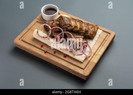 Schaschlik oder gegrillte Fleischrippchen mit Sauce und Zwiebel auf Pita auf Holzbrett Stockfoto