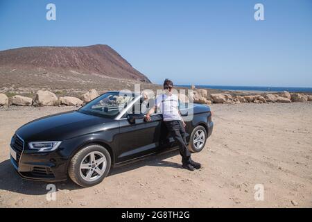 Lächelnder reicher Mann posiert mit seinem Cabrio, es ist Sommer, er ist im Urlaub am Strand und genießt das Leben. Stockfoto