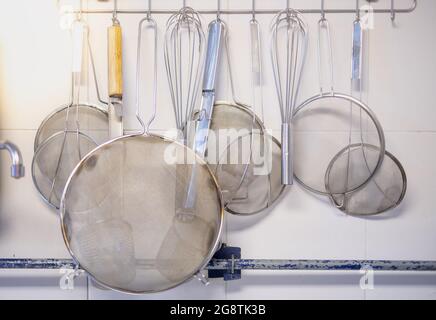 Verschiedene Küchenutensilien nach der Reinigung hängen an der Wand für die einfache Verwendung zum Kochen an den Koch. Stockfoto