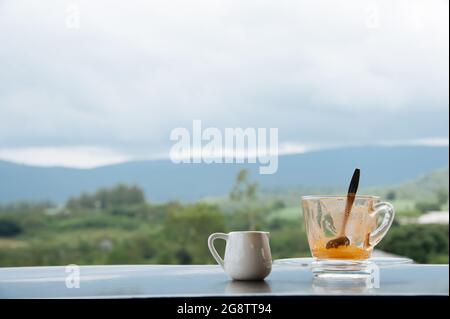 Heißer Thai-Milchtee in einer Tasse mit Blick auf die Berge, wenn es von weit her regnet Stockfoto