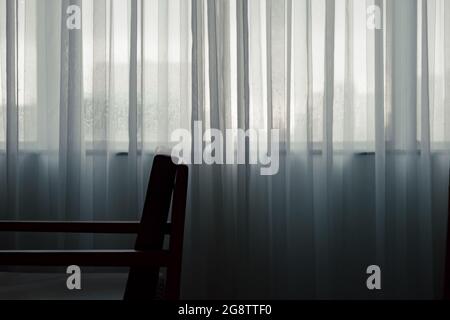 Ein Teil des Stuhls neben den Fenstern Vorhang in der dunklen Szene mit Regen machen Füllung einsam Stockfoto