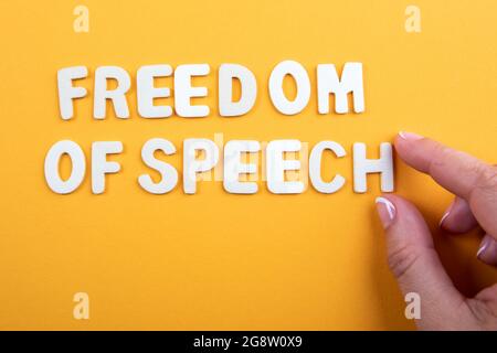 Redefreiheit. Weiße Buchstaben und die Hand einer Frau auf gelbem Hintergrund. Stockfoto