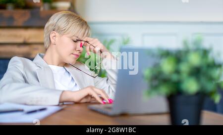 Nahaufnahme einer erschöpften Frau, die vor Ablauf der Frist zu Hause arbeitet. Eintreten für moderne Technologien im Alltag. Stockfoto