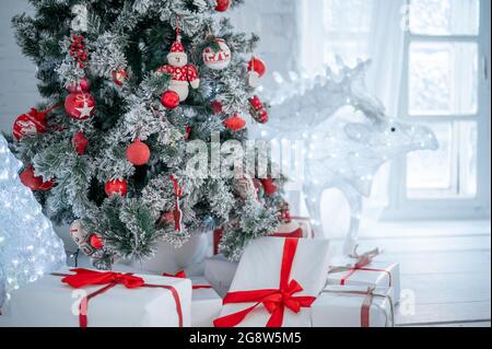 Weihnachtsbaum und Weihnachtsgeschenkschachteln im Innenraum mit Hirsch. weihnachtskarte. Weihnachtsbaum mit Spielzeug geschmückt, viele Geschenke mit rotem Band gebunden aro Stockfoto