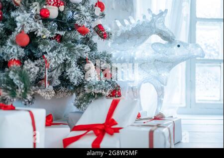 Weihnachtsbaum und Geschenkschachteln im Innenraum mit Hirsch. weihnachtskarte. Weihnachtsbaum mit Spielzeug geschmückt, viele Geschenke mit rotem Band um Christus gebunden Stockfoto