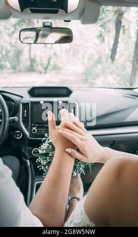 Bild von Mann und Frau in einem Auto.Junges Ehepaar hält Hände, Zeremonie Hochzeitstag. Vermählte die Hände des Paares mit Eheringen. Stockfoto