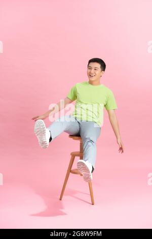 Ein junger, gutaussehender Mann mit T-Shirt saß auf einem Stuhl, der auf dem Hintergrund isoliert war Stockfoto