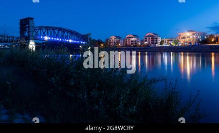 Magdeburg, Deutschland. Juli 2021. Die Liftbrücke im Stadtpark Rotehorn, eine ehemalige Eisenbahnbrücke, zur blauen Stunde. Rechts stehen moderne Mehrfamilienhäuser am Ufer der Elbe. Quelle: Stephan Schulz/dpa-Zentralbild/ZB/dpa/Alamy Live News Stockfoto