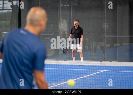 Überwachen Sie den Padel-Unterricht für den Mann, sein Schüler - Trainer lehrt Jungen, wie Padel auf dem Hallentennisplatz zu spielen Stockfoto