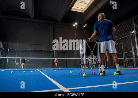 Überwachen Sie, wie Mann und Frau Padel lernen, seine Schüler - Trainer lehrt, wie man Padel auf dem Hallentennisplatz spielt Stockfoto