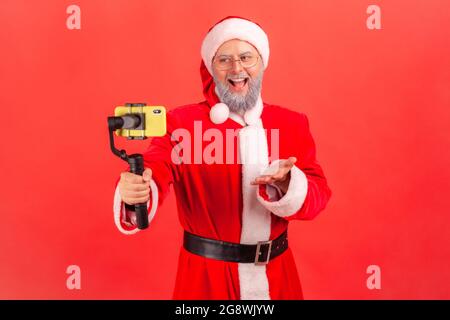 Glücklich positive ältere Mann mit grauem Bart trägt weihnachtsmann Kostüm Rundfunk Live-Stream, mit standicam, im Gespräch mit Anhängern. innenstudi Stockfoto