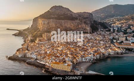 Sonnenaufgang über dem Hafen in Cefalu, Sizilien, Italien, Panorama-Luftaufnahme der Altstadt mit bunten Häusern am Wasser, Meer und La Rocca Klippe. Stockfoto