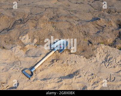 Der Plastikspaten eines Kindes mit einem Piraten-Thema auf der Klinge wurde an einem Sandstrand zurückgelassen. Eine Flut ist hereingekommen und hat den Sand verdunkelt. Stockfoto