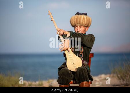 Kirgisischer Musiker, der in Issyk Kul, Kirgisistan, ein traditionelles Musikinstrument namens Komuz spielt Stockfoto