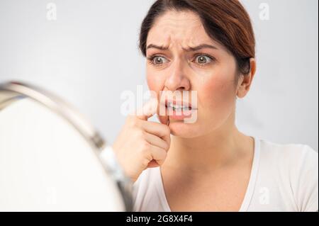 Kaukasische Frau schaut sich im Spiegel an und ist wegen der Gesichtsfalten auf ihrem Gesicht verärgert. Stockfoto