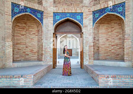 Usbekische Frau in einheimischer Kleidung mit dem Barak Khan Madrasa im Hintergrund Stockfoto