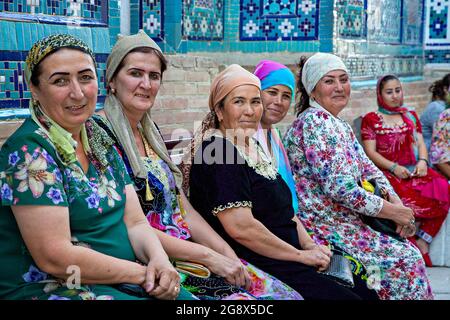 Frauen in bunten, traditionellen Kleidern sitzen und ruhen im Innenhof des Shahi Zinda Religious Complex in Samarkand, Usbekistan. Stockfoto