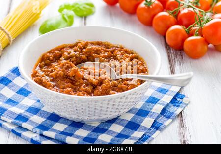 Authentisches italienisches Bolognese-Ragu aus Hackfleisch und Schweinefleisch, langsam zubereitet mit Tomatenmark, Olivenöl, Knoblauch und Rosmarin, serviert auf einer Schüssel auf einem zarten Whi Stockfoto