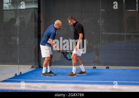 Überwachen Sie den Padel-Unterricht für den Mann, sein Schüler - Trainer lehrt Jungen, wie Padel auf dem Hallentennisplatz zu spielen Stockfoto