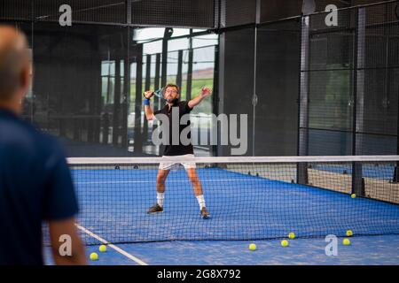 Überwachen Sie den Padel-Unterricht für den Mann, sein Schüler - Trainer lehrt Jungen, wie Padel auf dem Hallentennisplatz zu spielen Stockfoto