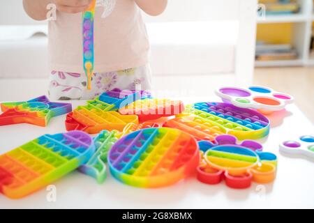 Kleines Mädchen, Kind, Kind spielt mit bunten Pop es Kinderzimmer, Schlafzimmer.Funny trendy Silikon Antistress bunte sensorische Push-Spielzeug popit.Flapping Fi Stockfoto