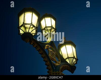 Einer der kunstvollen, im Stil der Gotik erleuchteten Lampenpfosten aus Eisenwerk an der Westminster Bridge, in der Nähe der britischen Parlamentsgebäude. Ein dunkler Himmel liegt dahinter. Stockfoto